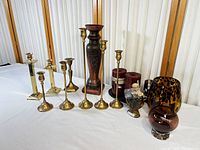 Photo showing full set of eight brass candlesticks, wooden holder, wax candles, and additional decorative holders on white surface.