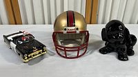 Full view of the lot showing mini 49ers helmet, CHP Santa car figurine, and black ceramic dog figurine on a white surface with wooden background