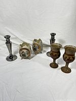 Photo showing the pair of silver-chrome tone candlesticks, two decorative footed vases with floral motifs, and two textured brown glass goblets