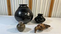 Full view of all four items including the large black vase, two smaller pottery vases, and the tribal animal figurine.