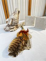 Photo showing the prayer feather fan with various natural feathers and beaded handle, placed alongside a gray-white howling wolf head sculpture and two squared ceramic plaques with textured relief designs.