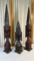 Three tall hand painted tribal face decorations with pointed tops and square bases, displayed together indoors.