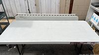 Photo of one of the plastic tables showing white textured tabletop and black metal folding legs.