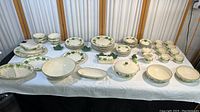 Full spread of Franciscan Ivy patterned dinnerware spread across two tables showing multiple plates, bowls, cups, serving bowls, and specialty pieces.