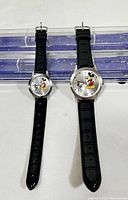 Front view of both Mickey Through The Years watches showing black leather straps and silver-tone faces with classic and modern Mickey Mouse images.