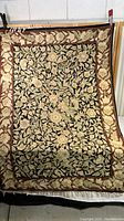 Full view of the tapestry showing the overall floral pattern with black center and brown border