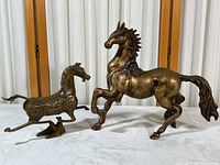 Two brass horse sculptures side by side showing different styles and size comparison