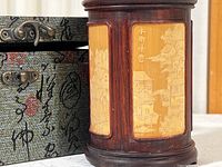 Photo showing carved bamboo cup with detailed scenic panels next to fabric covered storage box with metal latches.