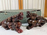 Pair of red-brown carved stone dragon figurines in front of green fabric-covered box