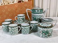Full service set with pot, sugar bowl, cream pitcher, six cups and saucers, displayed on white cloth with orange storage box in background.