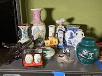 Full view of the lot showing multiple Asian vases, figurine, hand-painted eggs in glass case, wooden eagle carving, Dutch wooden ship model, and Dutch shoes.