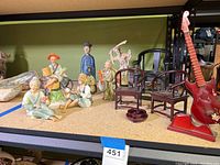 Overview of all items arranged on shelf: six Far Eastern-style figures in various poses, three miniature wooden chairs, a small red wooden guitar, and a round wooden display stand.