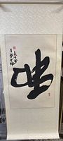 Full view of the Asian hanging scroll showing black calligraphy on textured paper with beige floral border.