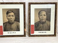Pair of vintage black and white portraits of an Asian man and woman in ornate gold-colored frames with red paper labels on front.