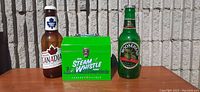Front view of the three items showing Molson Canadian plastic beer bottle bank, Steam Whistle green metal box, and Moosehead Lager plastic beer bottle bank side by side.