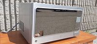Silver GE microwave oven with mirrored front and digital keypad on right side, shown in outdoor setting.