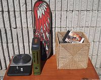 Xbox 360 console with green and orange custom skin next to DJ Hero turntable and a basket containing multiple video game cases including Skyrim, with a Tony Hawk skateboard deck behind.