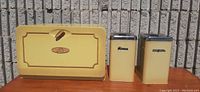 Set of yellow vintage Kenmore metal canisters and matching bread box against a background of textured concrete blocks