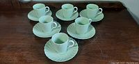 Photo showing six demitasse cups each placed on its matching saucer with shell pattern design in pale green glaze.
