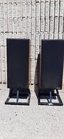 Pair of Paradigm 7se speakers with black grille covers on stands, photographed outdoors against a textured wall.