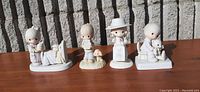 Front view of 4 Precious Moments porcelain figurines on a wooden surface in front of a stone wall.