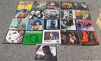 Full view of 21 vinyl record albums laid out on pavement in rows, showing colorful covers and various artists.
