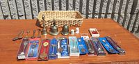 Full lot displayed on table under sunlight showing all souvenir spoons, brass bells, basket and other small items