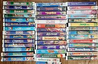 Photo showing front and top views of VHS tape spines including Disney classics like Robin Hood, Bambi, Tarzan, Jungle Book, Aladdin and others.
