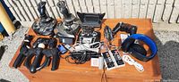 Table with various gaming controllers and joysticks laid out outside in sunlight.