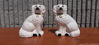 Front view of both white ceramic mantel dogs sitting side by side, showing detailed sculpted fur and facial features.