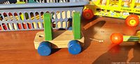 Photo showing wooden pull toy with blue wheels and green handles on a wooden surface