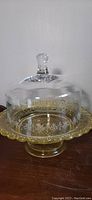 Side view of yellow glass compote cake plate with clear glass dome on top, showing the floral etching on the dome.