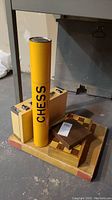 Photo of two chess sets and wooden box including yellow chess piece tube labeled 'CHESS'