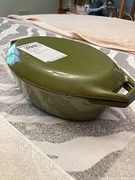 Olive green Copco casserole dish with lid on table showing side profile and lid handle