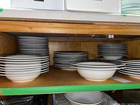 Shelves containing stacks of white bowls and plates with plain rims.