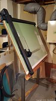 Drafting table viewed from front, showing green surface with black edging and an adjustable straightedge ruler.