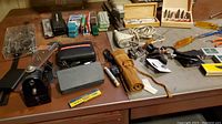 Overview of desk surface showing black RPM case, gray plastic case, leather tool roll, micrometer case, assorted small hand tools