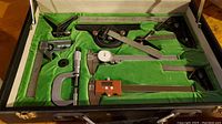 Overview of open case showing calipers, micrometer, rule and square heads on green felt