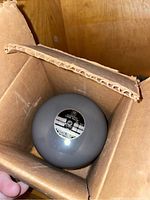 Grey spherical oscillator inside a cardboard box showing label and specifications