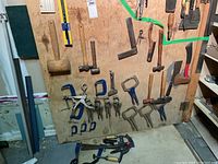 Full view of wooden board with assorted hammers and clamps mounted, tools including mallet, hammers, C-clamps, and locking pliers clamps.