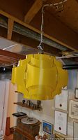 Front view of yellow plastic hanging lamp shade suspended from chain in basement setting.