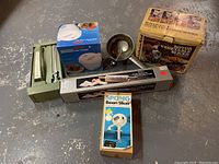 Overview of all kitchen items including electric carving tool, microwave rice cooker in box, rotary vegetable slicer in box, bean slicer box, large slicer knife, and metal masher.