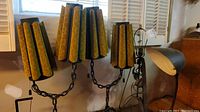 Pair of vintage table lamps with yellow velvet shades on black metal stand with chain and claw feet in front of white window shutters.