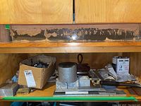 Wide view of wooden shelving unit holding a variety of metalworking tools, scrap metal pieces, and hardware components showing metal blocks, measuring tools, and a container of Cool-Tol.