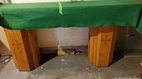 Two solid oak altar pillars under a tabletop, showing their octagonal shape and etched crosses, situated in an indoor setting with visible concrete floor