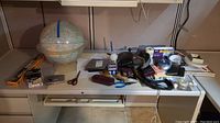Wide view of lot items arranged on white desk including globe, scissors, tape, and assorted small items