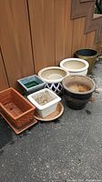 Photo showing the full set of seven assorted planters and pots arranged outside against a wooden wall, highlighting variety in size and materials.