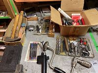 Tools including hammers, hand drills, taps, and assorted small tools arranged on a workbench and in trays.