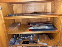 Wooden cabinet shelves containing various scrap metal pieces and small tools, metal sheets in various colors and sizes on middle shelf.