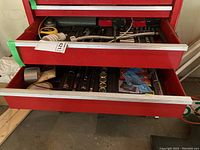 Photo of partially open red tool chest drawers showing chrome socket sets and accessories inside with some tools and boxes visible